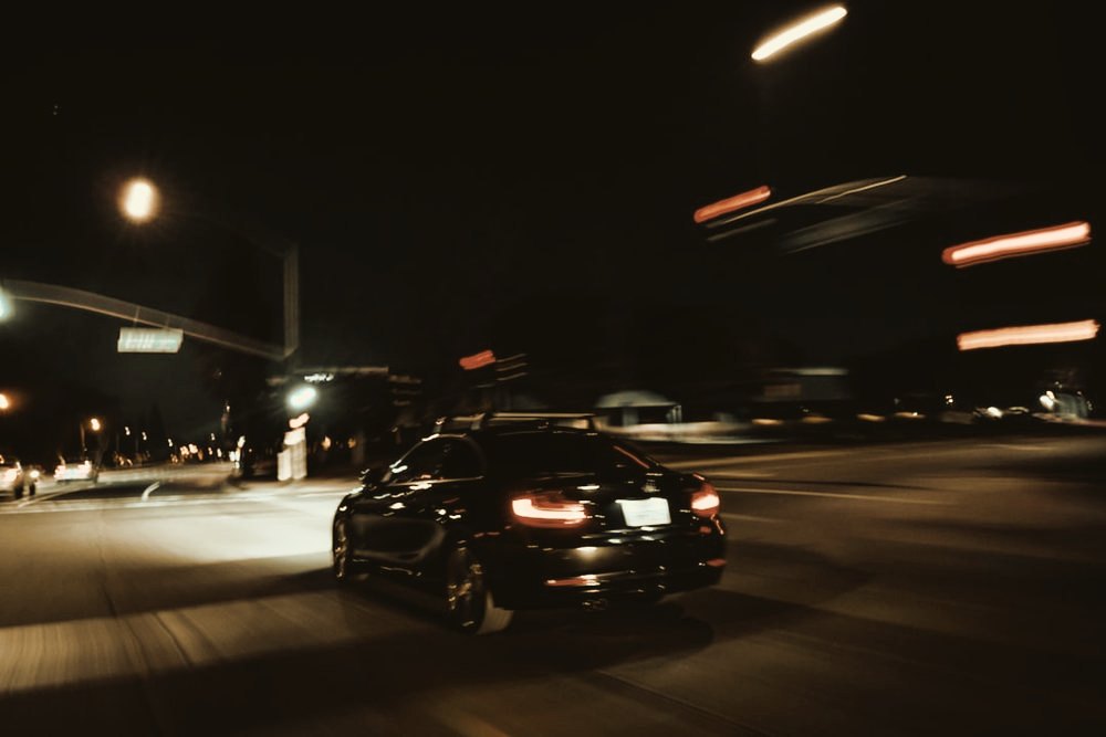 A car blurred with speed on a night road under streetlights